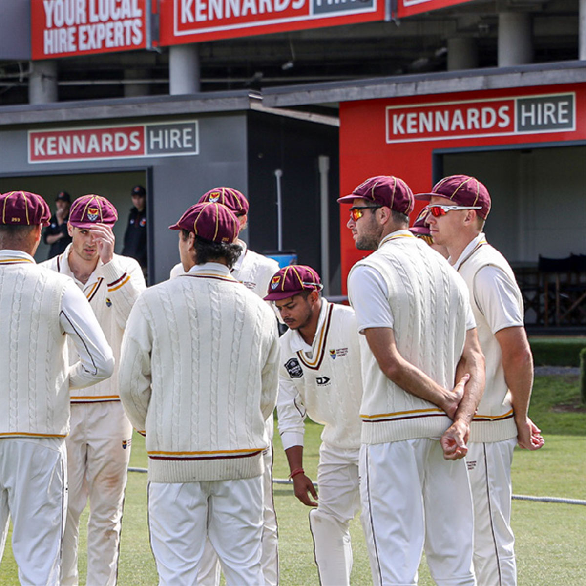 Cricket players chatting on pitch, with Kennards Hire signage in background