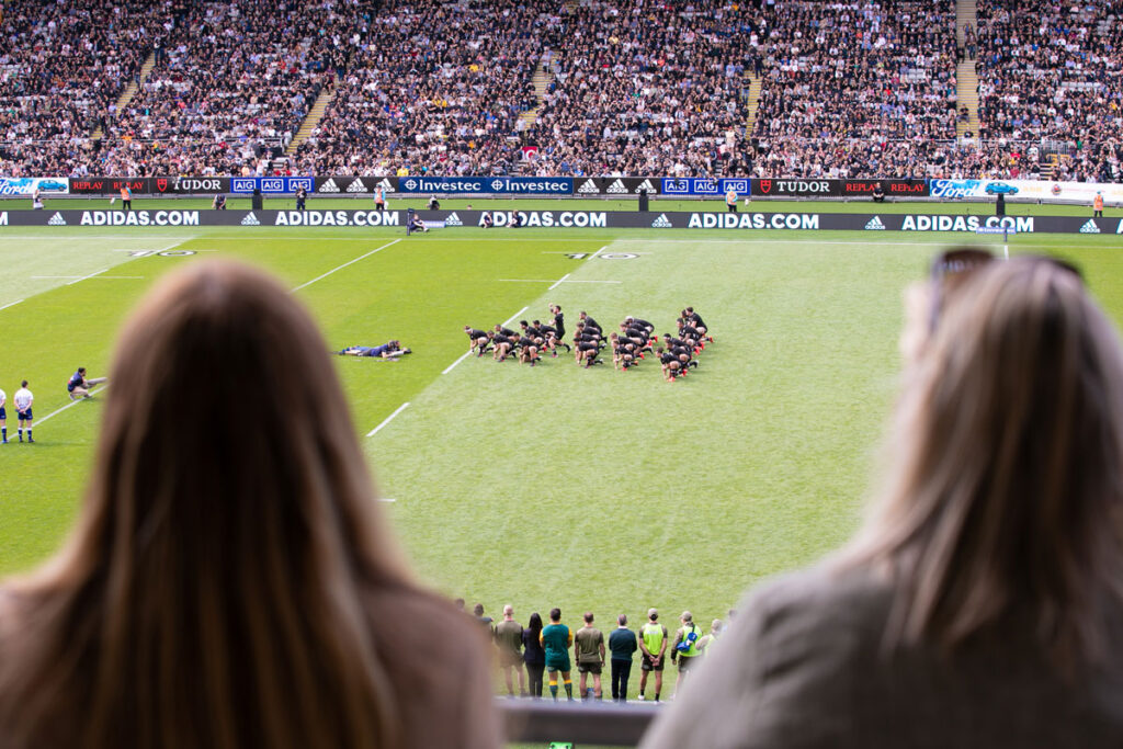 Two people watching all blacks from suite